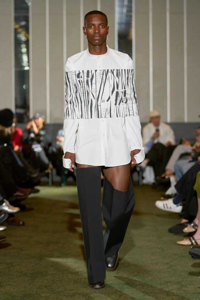 A fitted white shirt with a printed design paired with fitted black pants, featuring an asymmetric cut.
