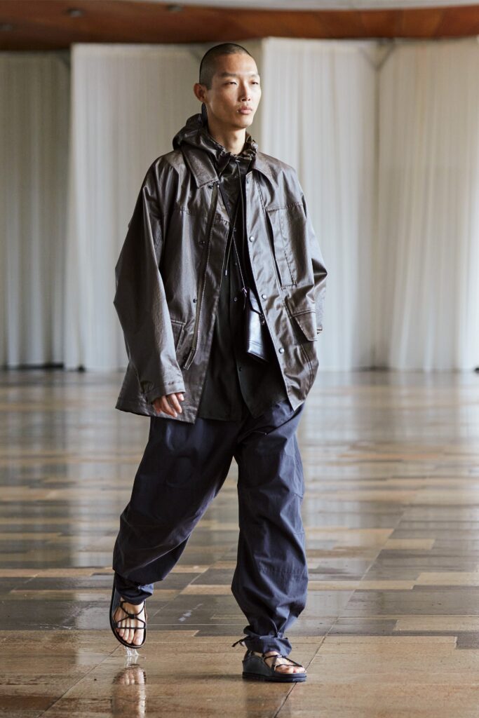 A relaxed-fit gray hooded jacket paired with black pants featuring zippered and buttoned details.