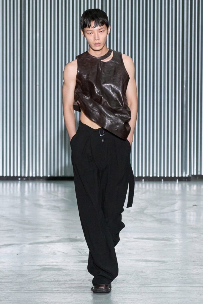 A fitted brown leather sleeveless top paired with relaxed black high-waisted pants.