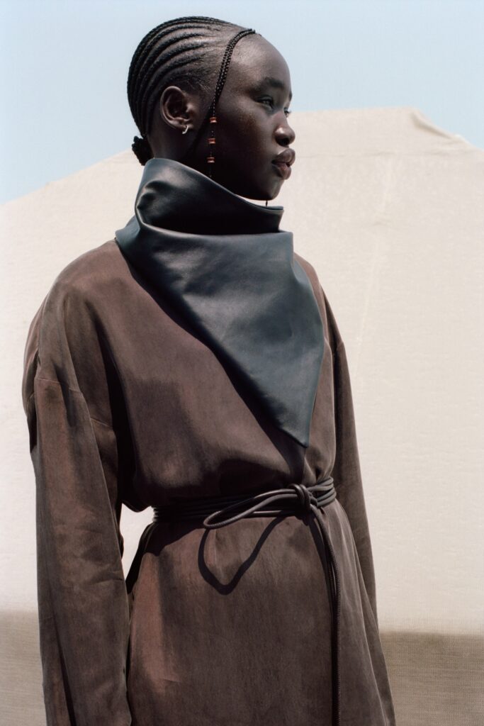 A fitted brown leather dress with long sleeves, a high neckline, and a belted detail.