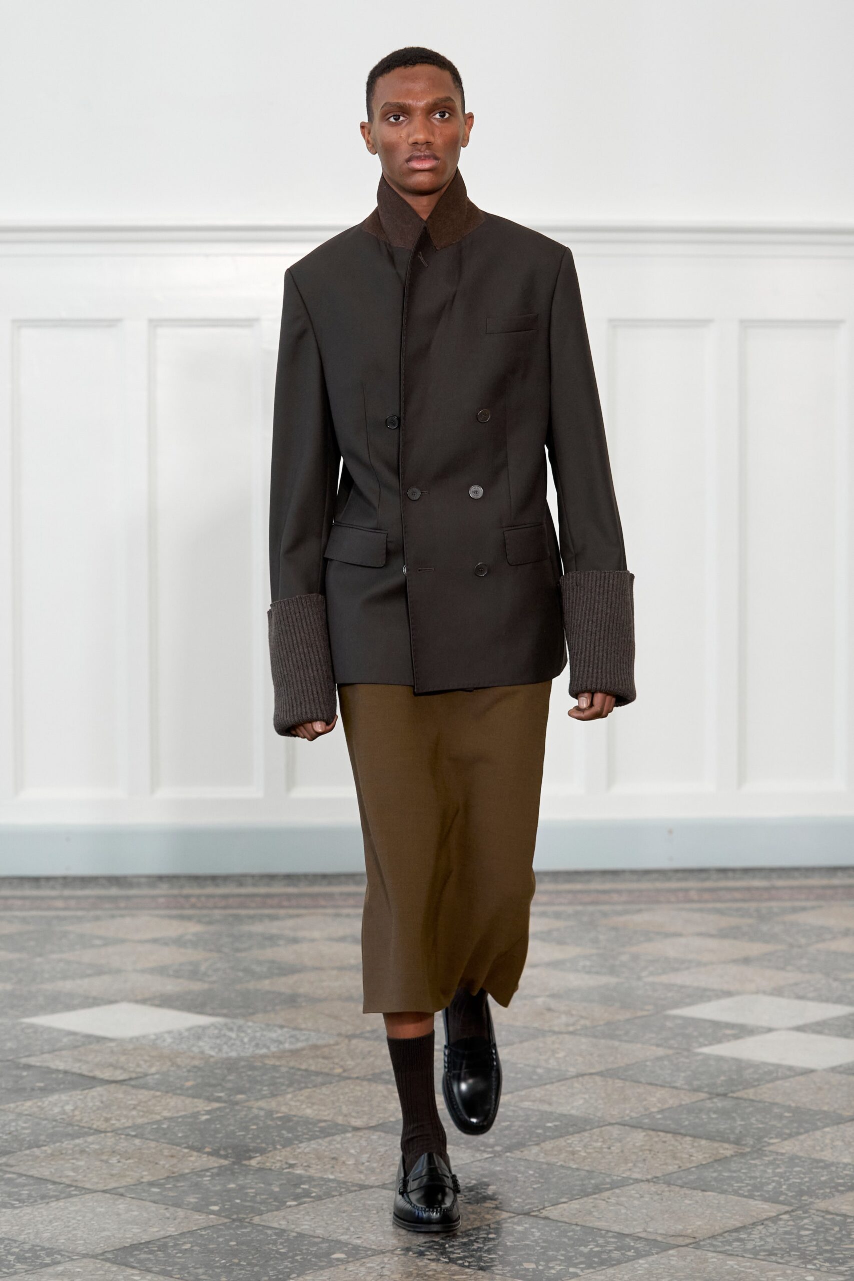A fitted black jacket with long sleeves and a collared design paired with a brown skirt.