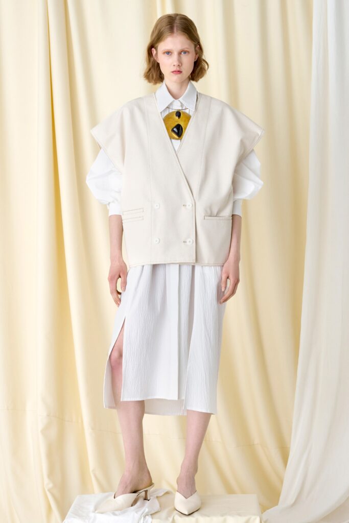 A relaxed white vest layered over a dress with long sleeves and an asymmetric slit.