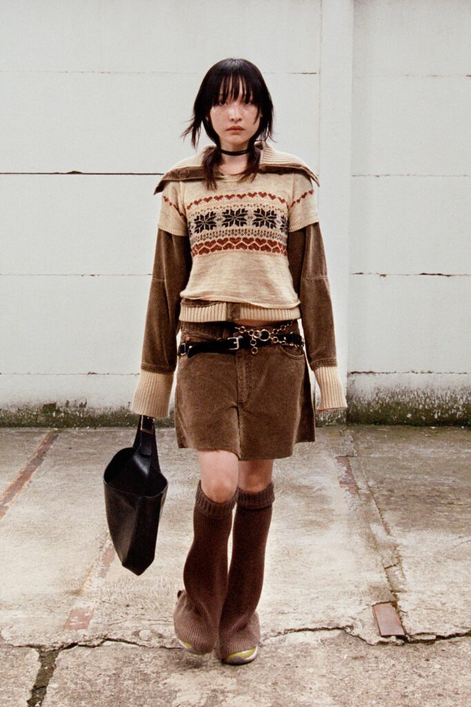A fitted brown sweater with long sleeves and a collared design paired with a mini skirt.