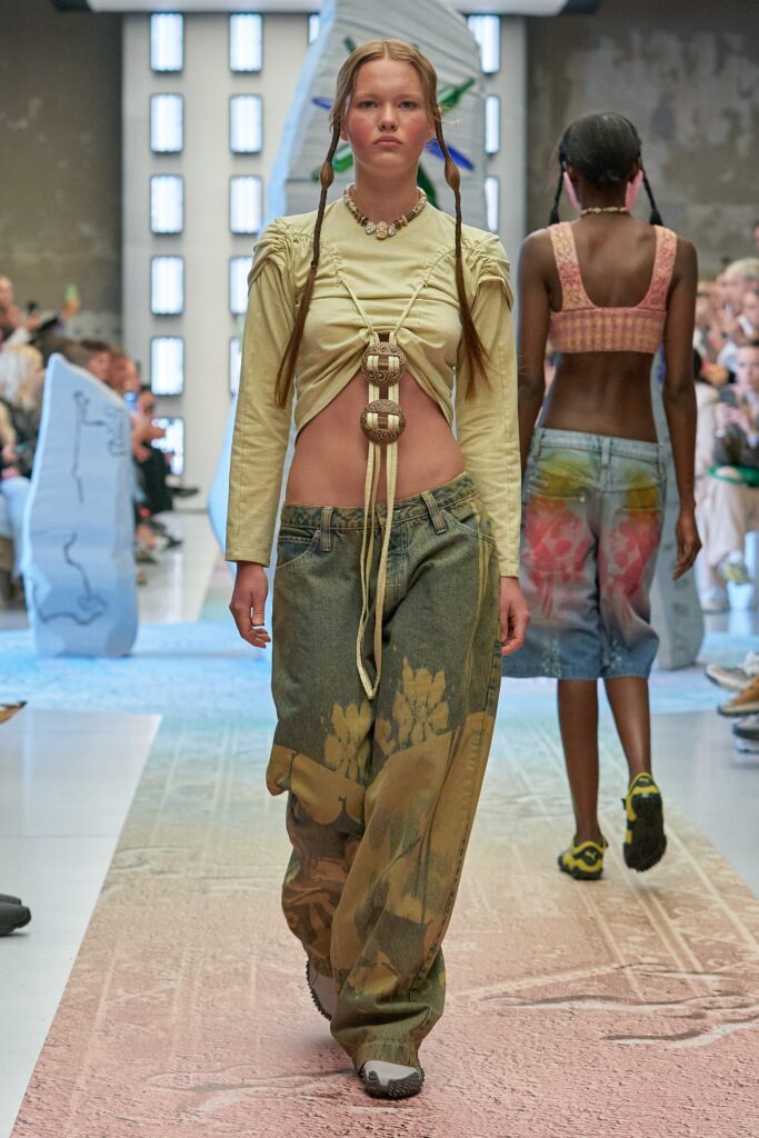 A relaxed beige cropped long-sleeve top paired with printed blue pants for a unique runway look.