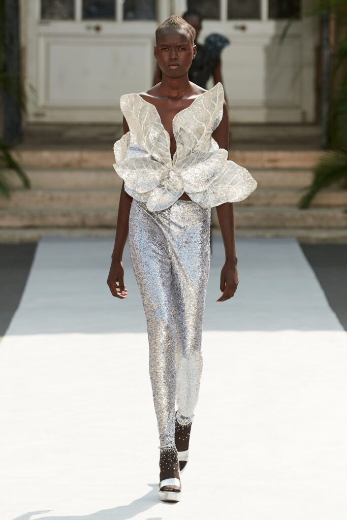 A fitted silver sequin sleeveless top with an asymmetric design paired with fitted pants.