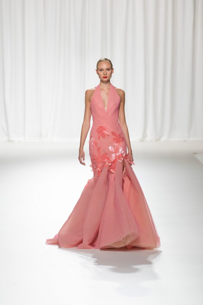 A fitted pink silk gown with a V-neckline and flared silhouette, adorned with floral details.