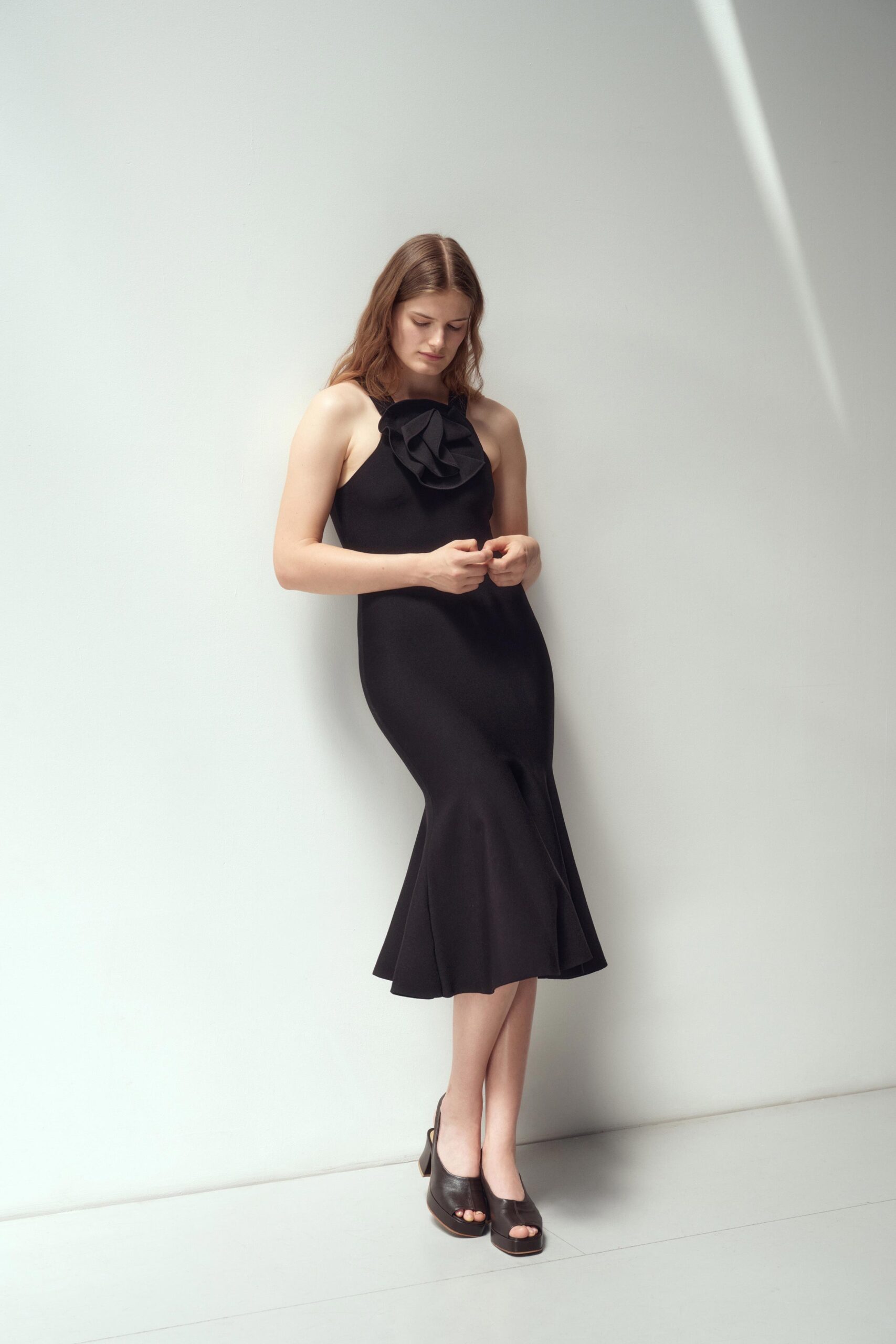 A fitted black sleeveless dress with a high neckline and flared silhouette.