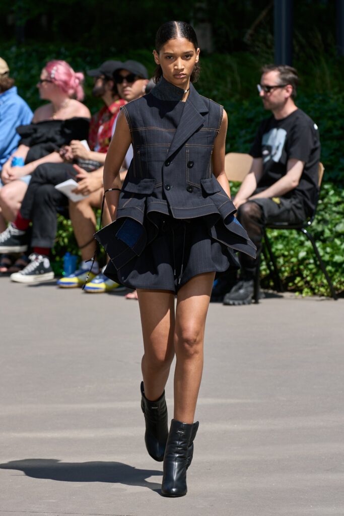A fitted black sleeveless blazer with an asymmetric layered design paired with shorts.