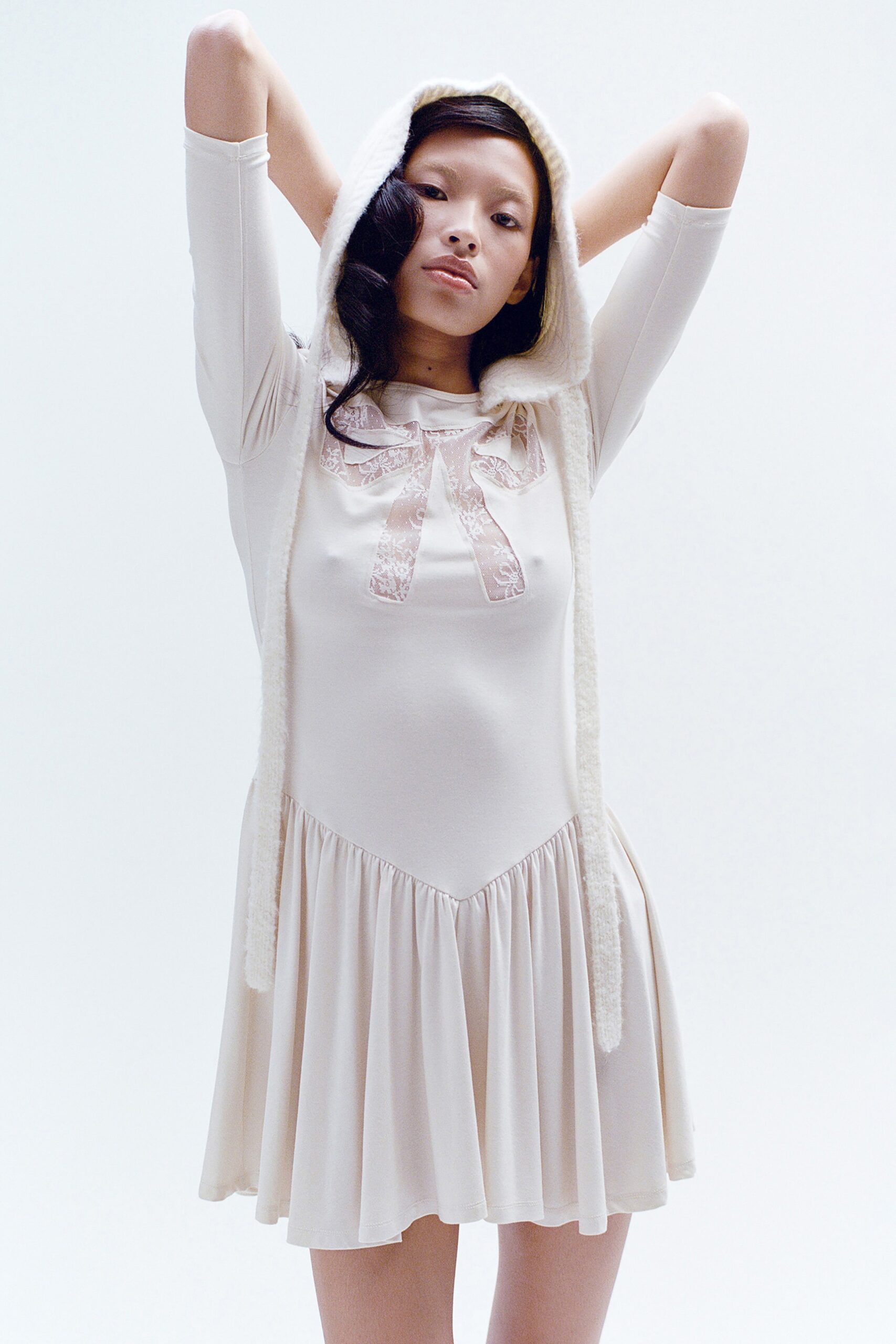 A relaxed cream dress with long sleeves, a hood, and pleated details.