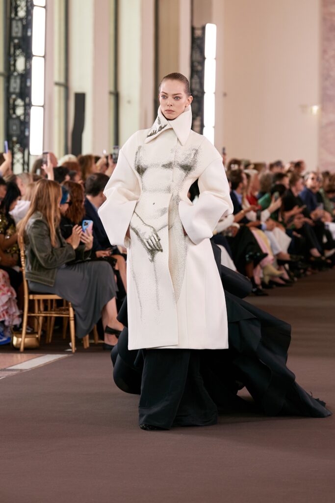 A fitted white silk coat dress with long sleeves and an asymmetric design.