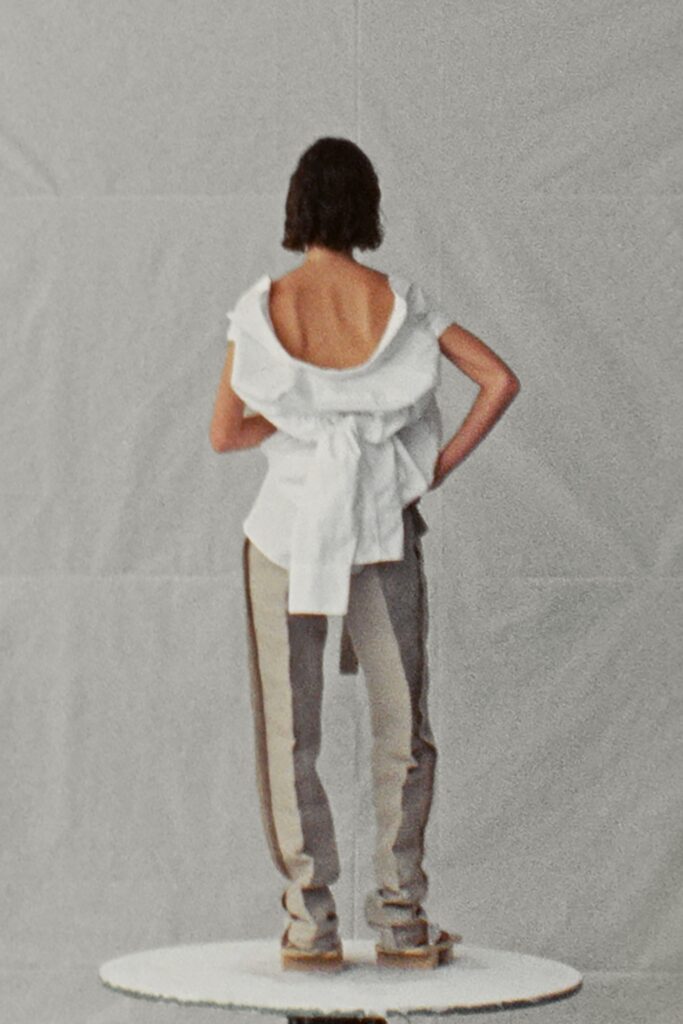 A relaxed white sleeveless top with a layered design paired with gray pants.