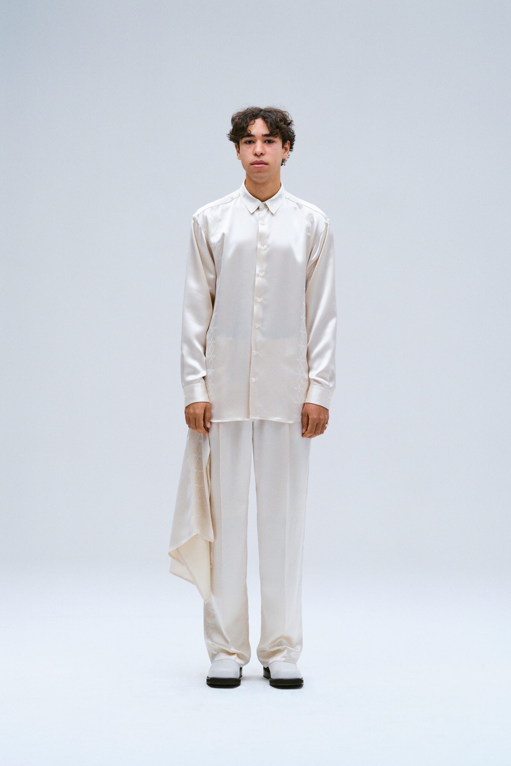 A relaxed cream silk long-sleeve shirt with a collared neck and asymmetric design paired with matching pants.