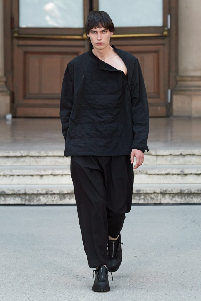 A relaxed black shirt with an asymmetric design paired with loose-fitting black pants.