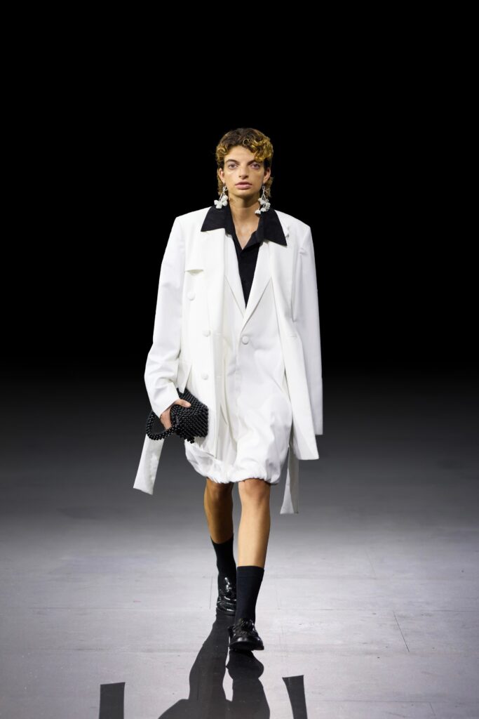 An oversized white blazer dress with a black shirt underneath and stylish accessories.