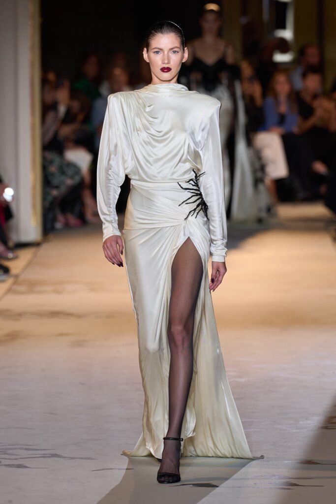 A fitted white silk dress with long sleeves, high neckline, and a dramatic slit.