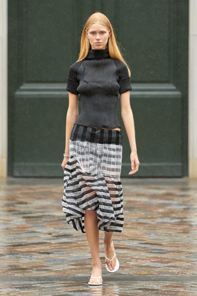 A fitted black top with a high-neck and short sleeves paired with a sheer asymmetric striped skirt.