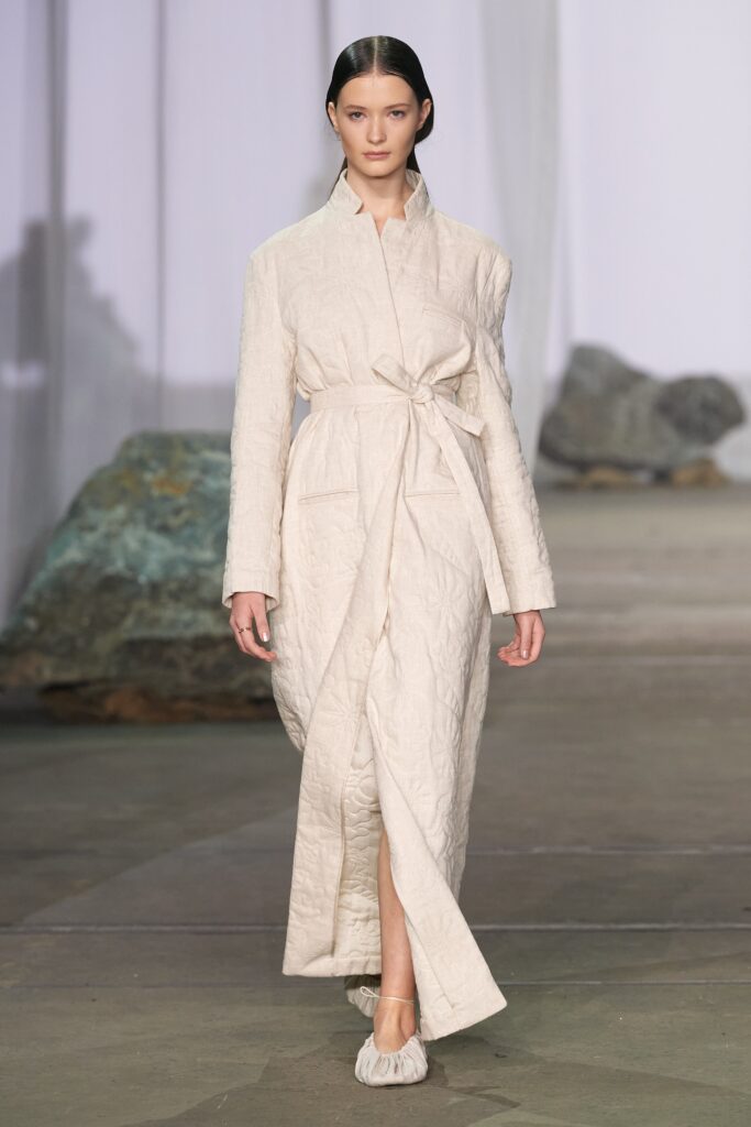 A relaxed beige cotton dress with long sleeves, a collared neckline, and a belted maxi silhouette.