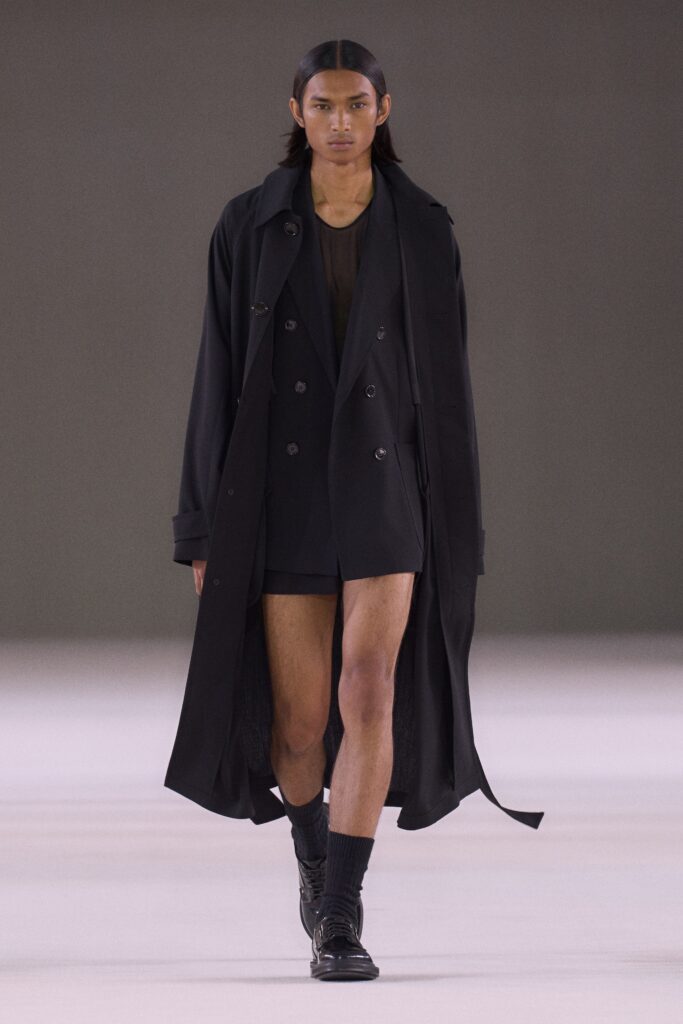 A fitted black coat dress with an asymmetric design and long sleeves.