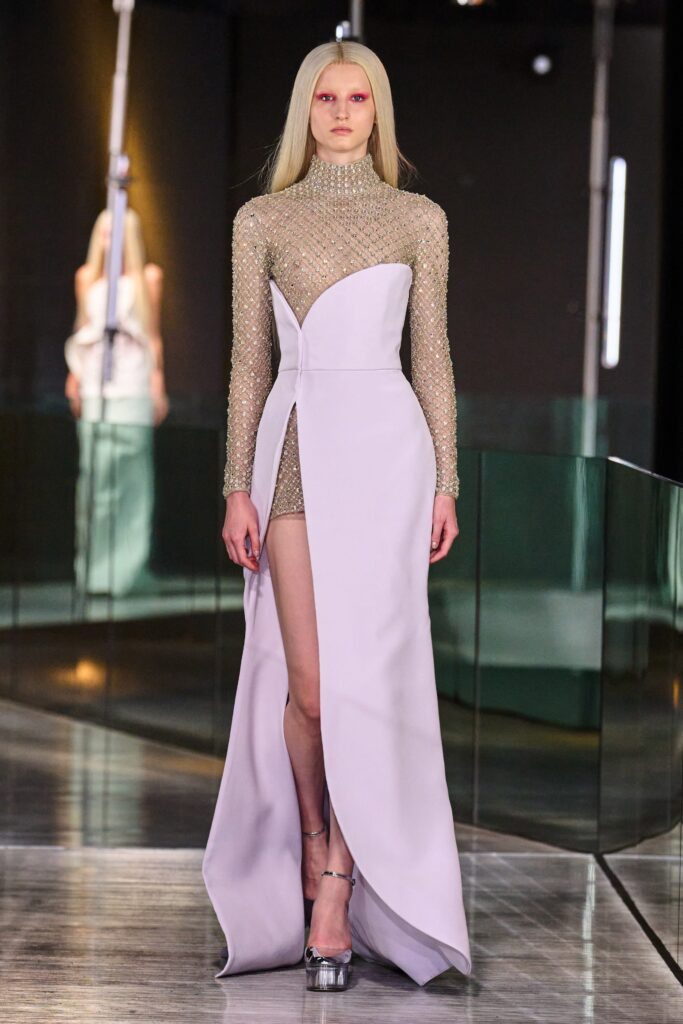 A fitted purple silk dress with long sleeves, a high neckline, and an asymmetric silhouette featuring a slit.