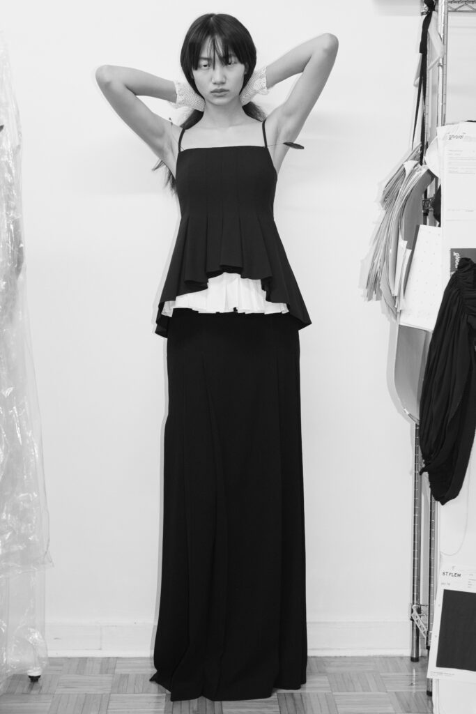 A fitted black sleeveless dress with a high neckline and layered design.