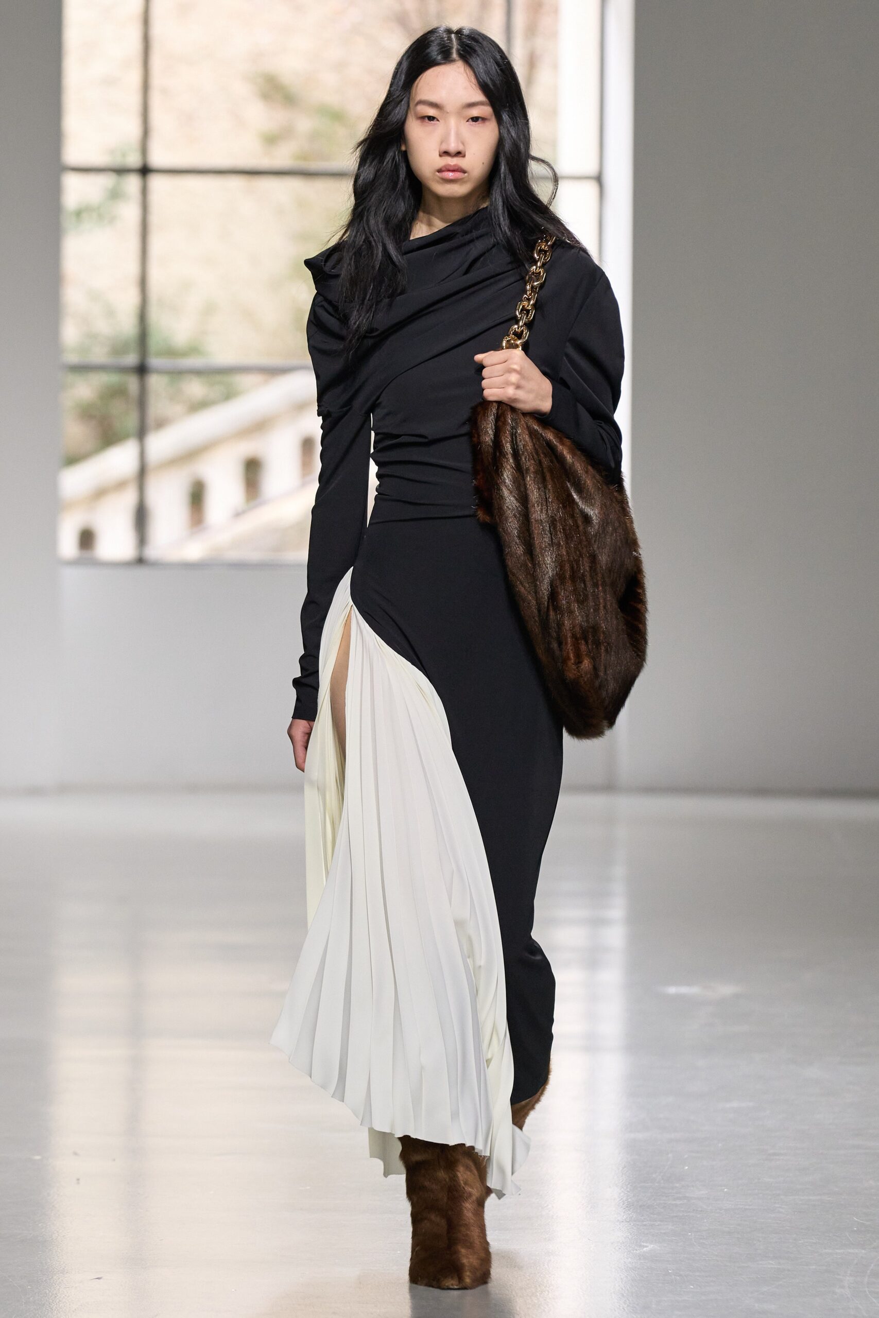 A fitted black and white dress with long sleeves, a V-neckline, and an asymmetric pleated design.