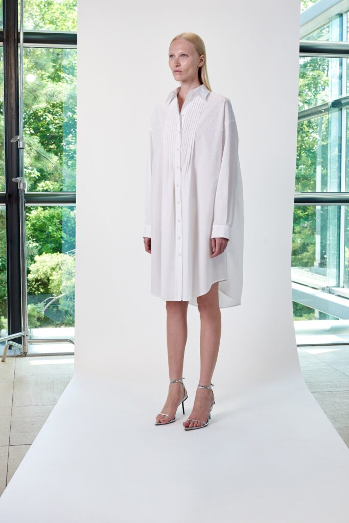 A relaxed white cotton shirt-dress with long sleeves and a collared neckline, featuring button details.