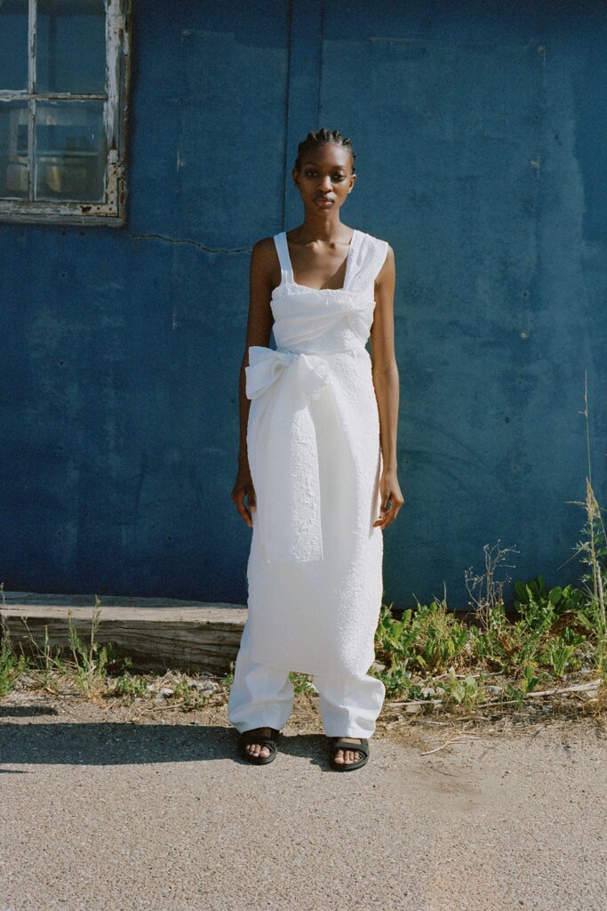 A fitted white sleeveless dress with a V-neckline and belted detail.
