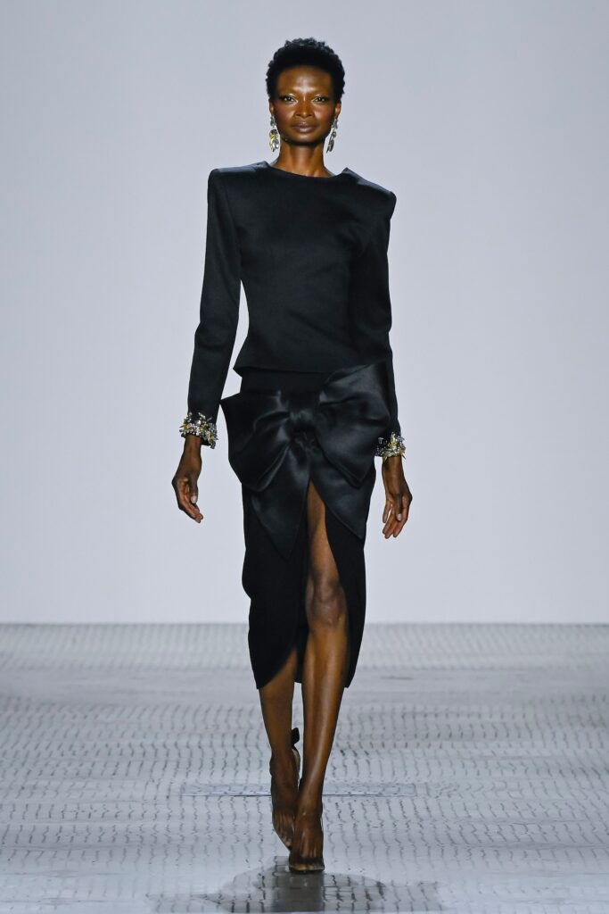 A fitted black silk dress with long sleeves, a V-neckline, and an asymmetric slit detail.