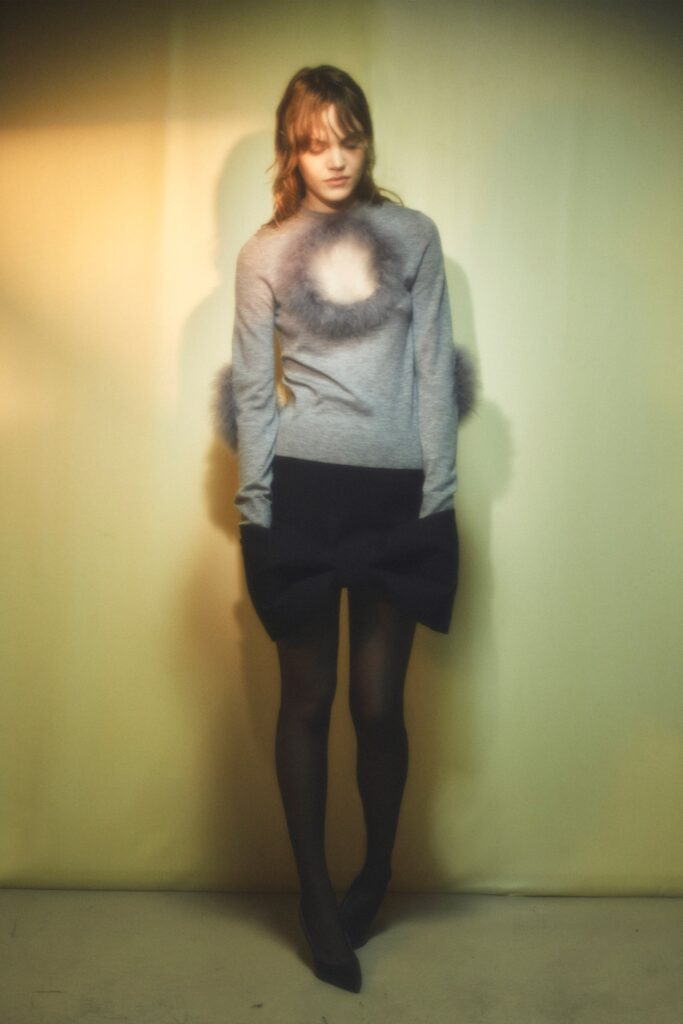 A fitted gray top with long sleeves and a cutout detail, paired with an asymmetric black skirt.