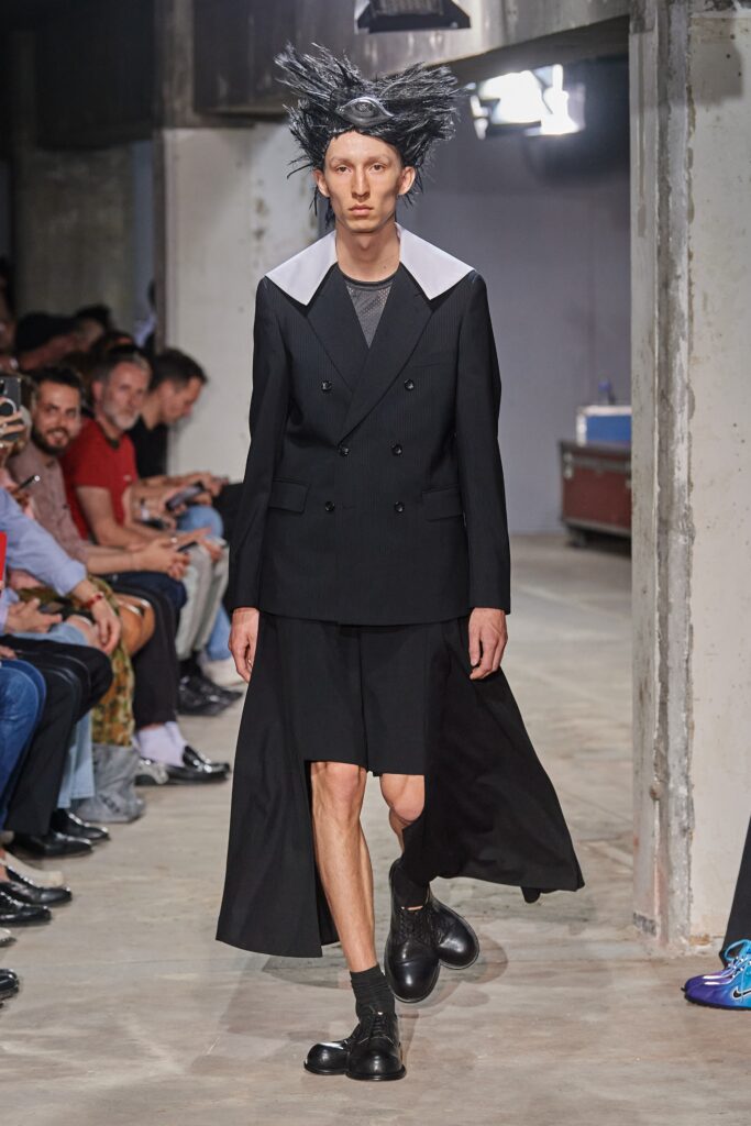 A relaxed black coat with a long-sleeve, collared design and an asymmetric skirt.