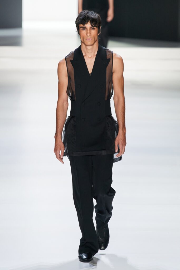 A fitted black silk sleeveless jacket with an asymmetric design and collared detail.