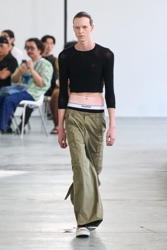 A fitted black long-sleeve cropped top paired with wide-leg green pants.
