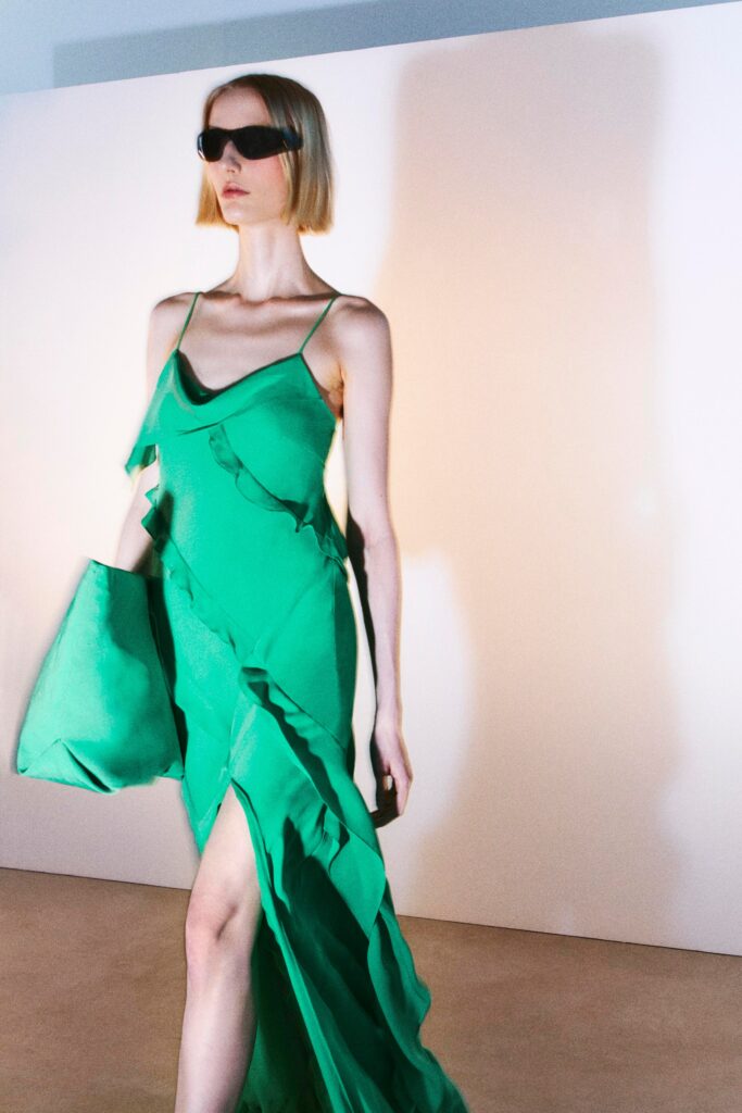 A fitted green silk dress with a sleeveless design, V-neckline, and asymmetric silhouette featuring a slit.