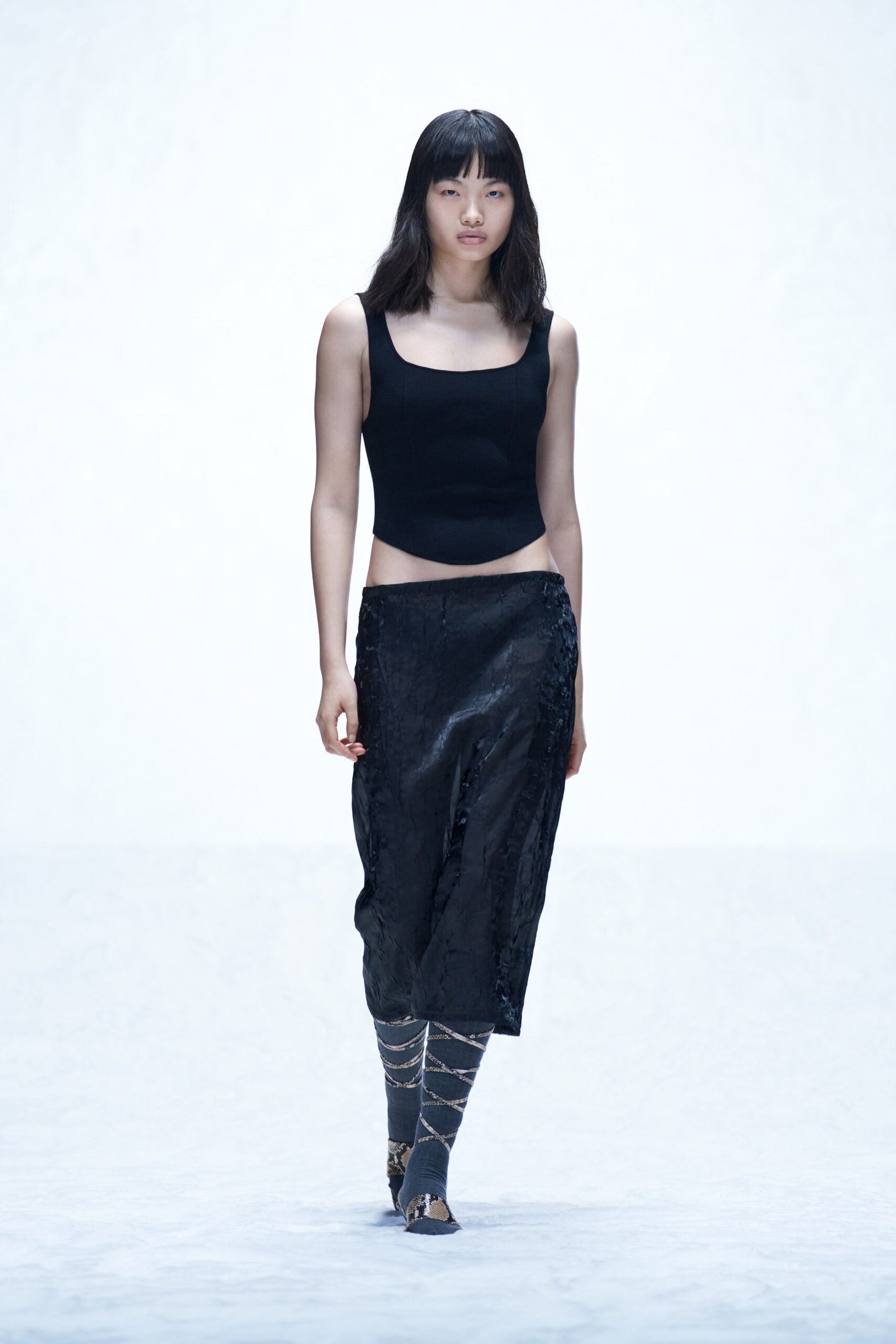 A fitted black silk sleeveless top paired with an asymmetric black skirt.