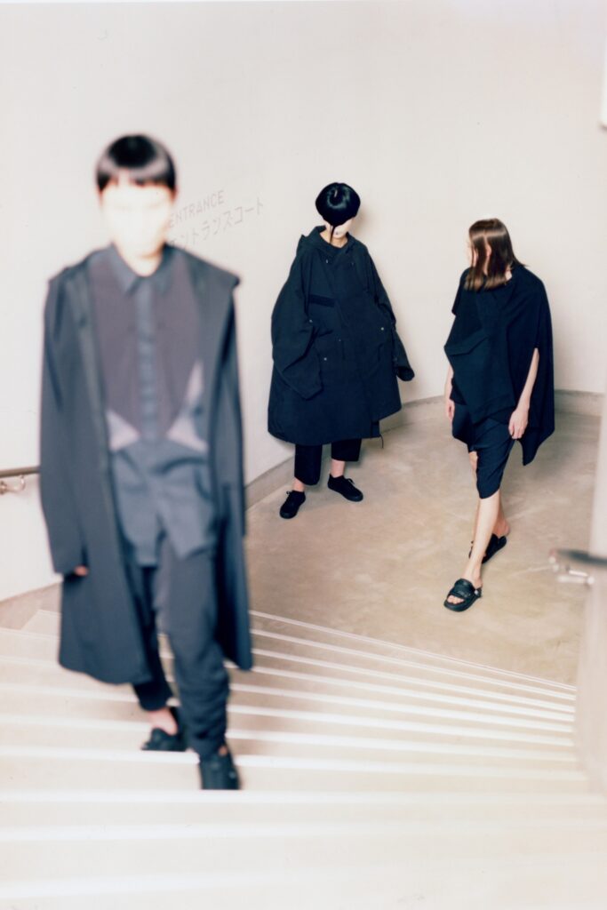 An oversized black coat dress with a sleeveless design and asymmetric detailing.