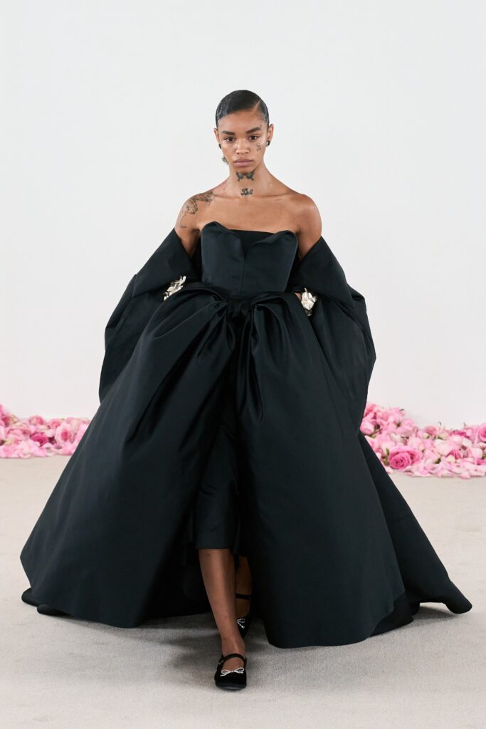 A fitted black silk strapless dress with a layered silhouette and a dramatic coat.