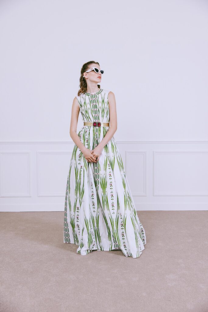 A fitted white dress with green floral patterns, featuring a high neckline and flared silhouette.