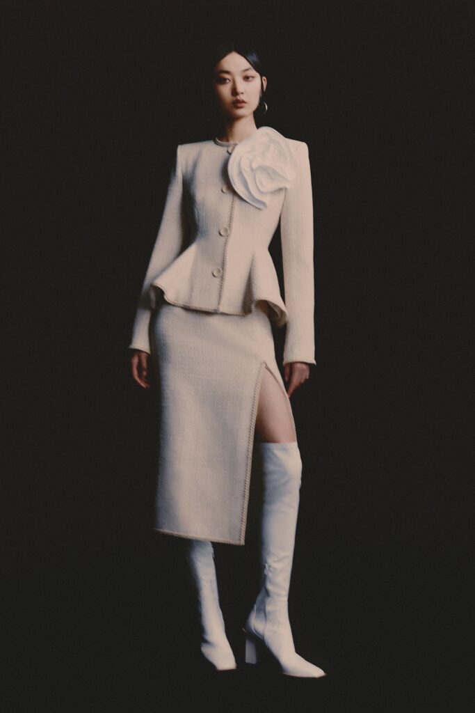 A fitted beige tweed blazer with a long sleeve and asymmetric skirt featuring a slit.