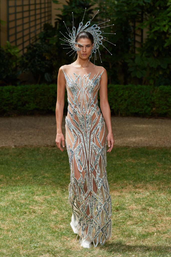 A fitted white sheer dress with intricate embroidery, featuring a sleeveless design and V-neckline.