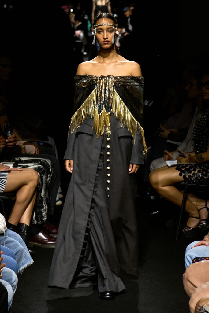 A fitted black silk off-shoulder dress with fringed details and button embellishments.