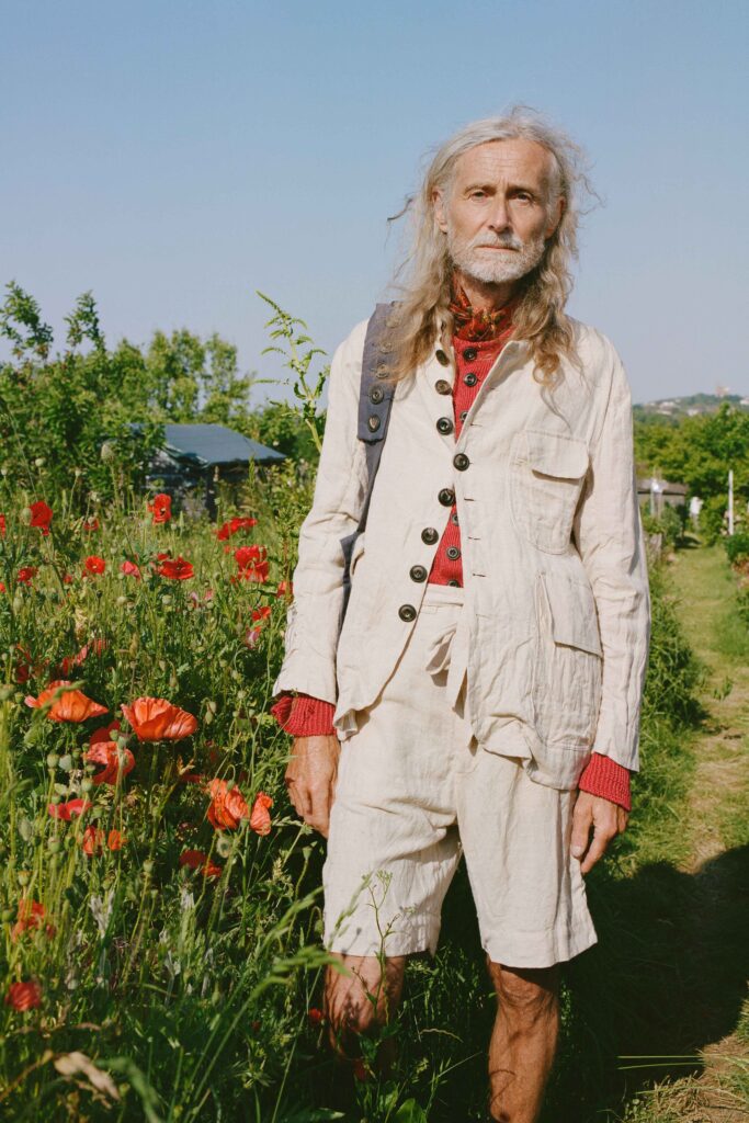 A relaxed-fit beige cotton suit paired with a long-sleeve red shirt and buttoned details.