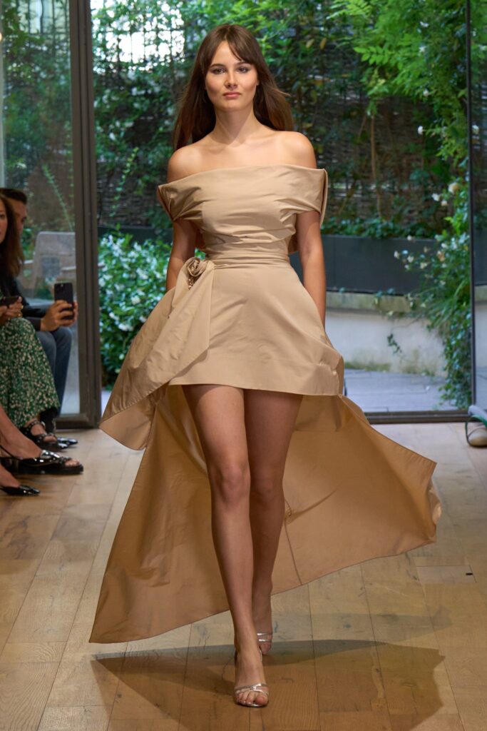 A fitted beige silk off-shoulder dress with an asymmetric hemline.