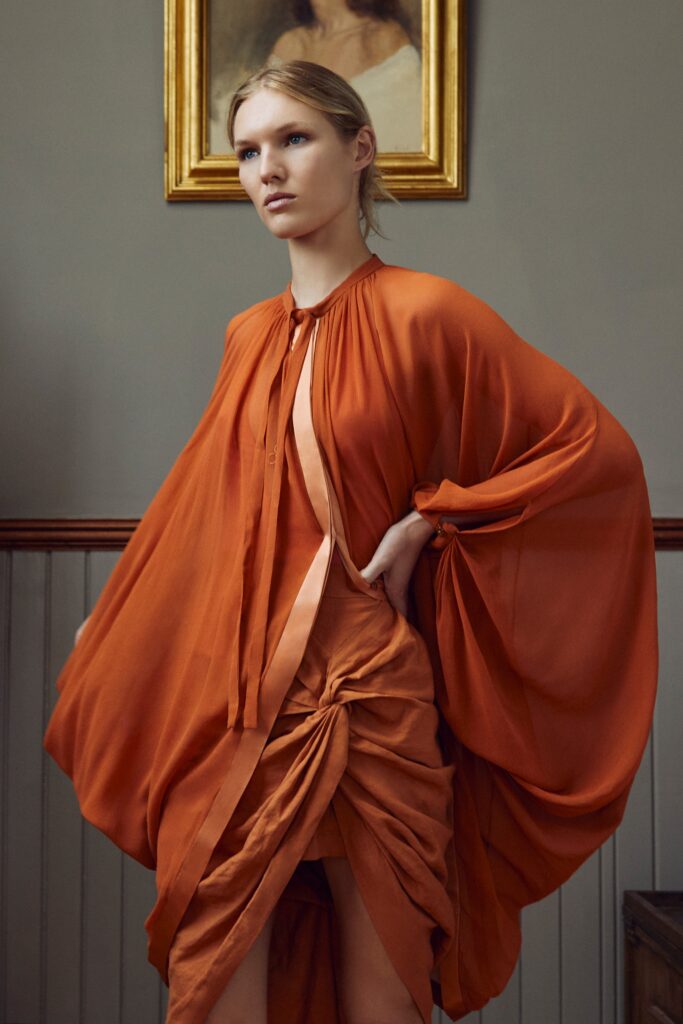 A relaxed orange silk dress with a V-neckline and asymmetric draped design.