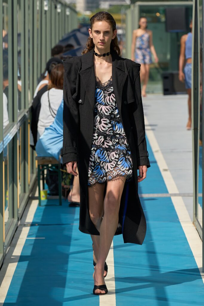 A fitted black sleeveless dress with a V-neckline and flared silhouette, paired with a stylish coat.