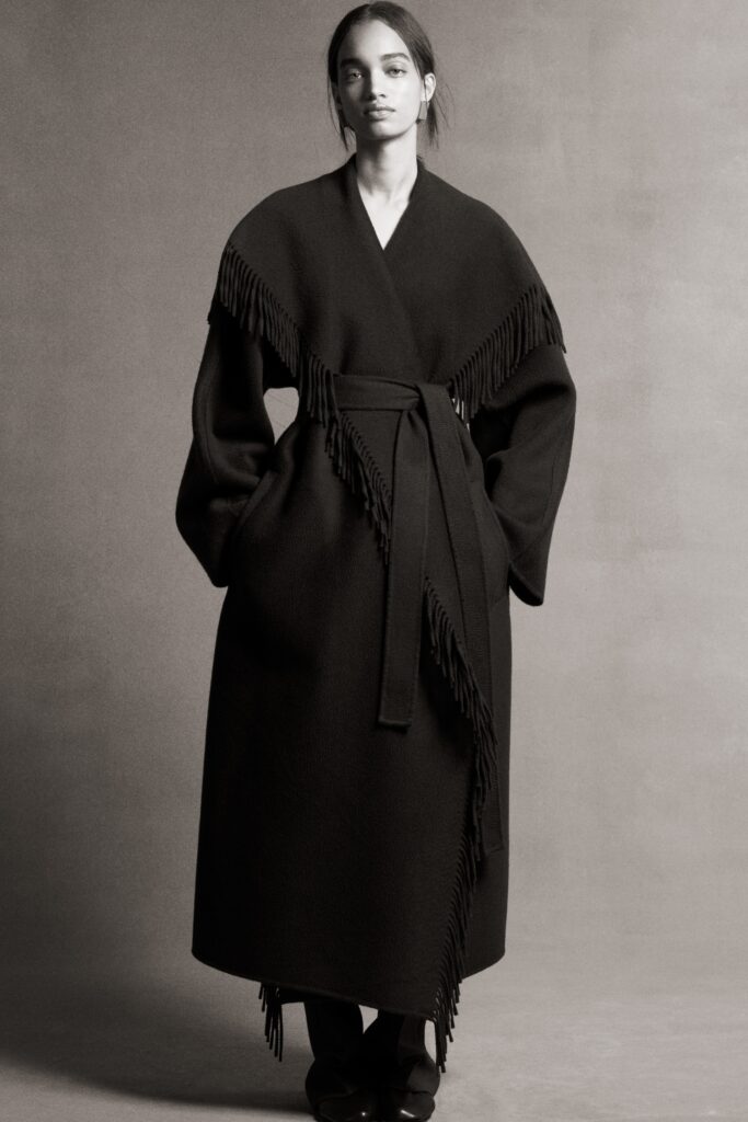 A relaxed black wool coat with long sleeves, a collared design, and fringed details.