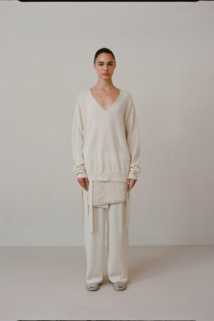 A relaxed cream wool sweater with a V-neck and layered design paired with matching pants.