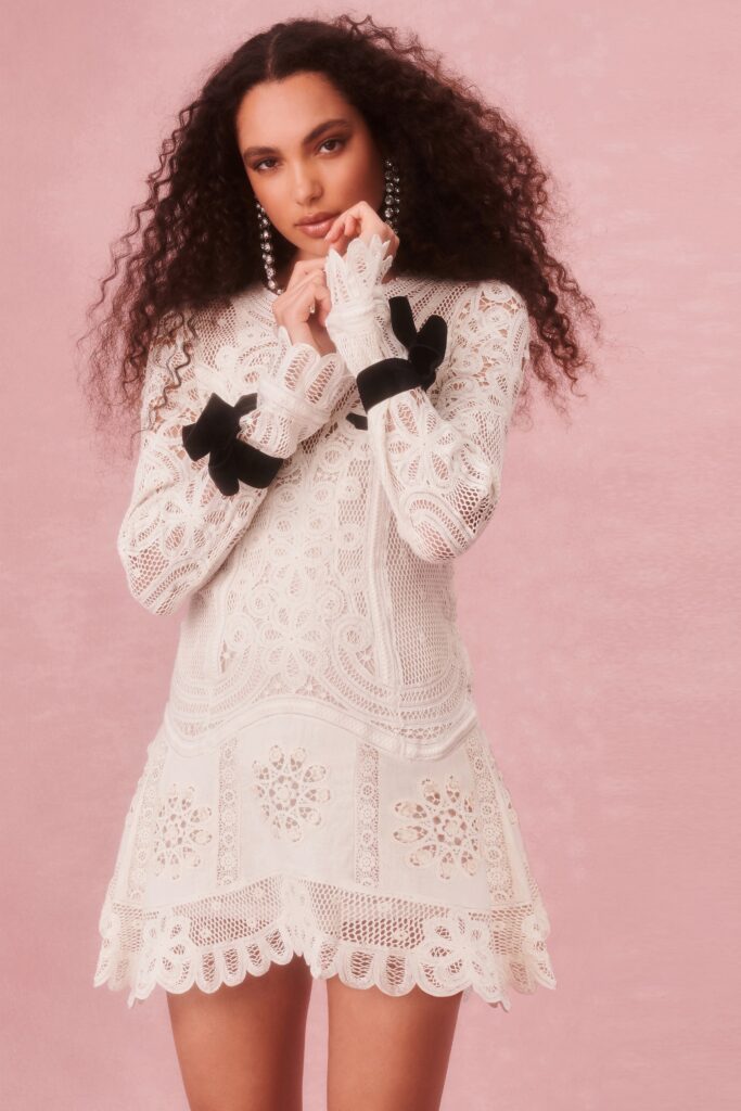 A fitted white lace dress with long sleeves, a V-neckline, and embroidered tiered details.