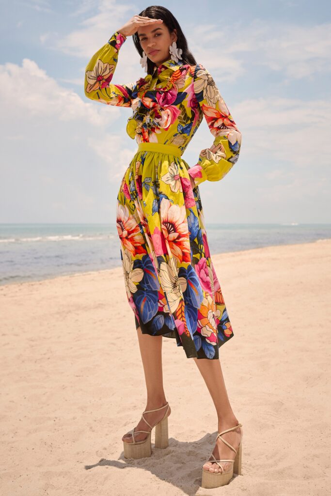 A fitted yellow dress with long sleeves, a collared neckline, and a flared silhouette featuring vibrant floral patterns.