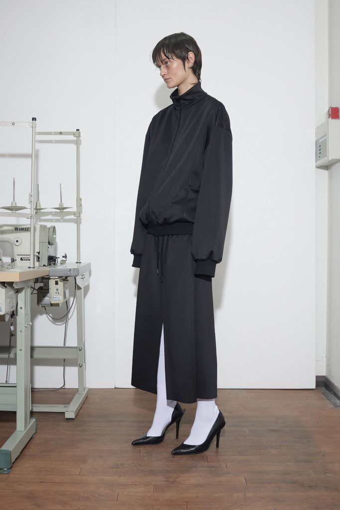 A relaxed black jacket with long sleeves and a collared design, paired with an asymmetric skirt.
