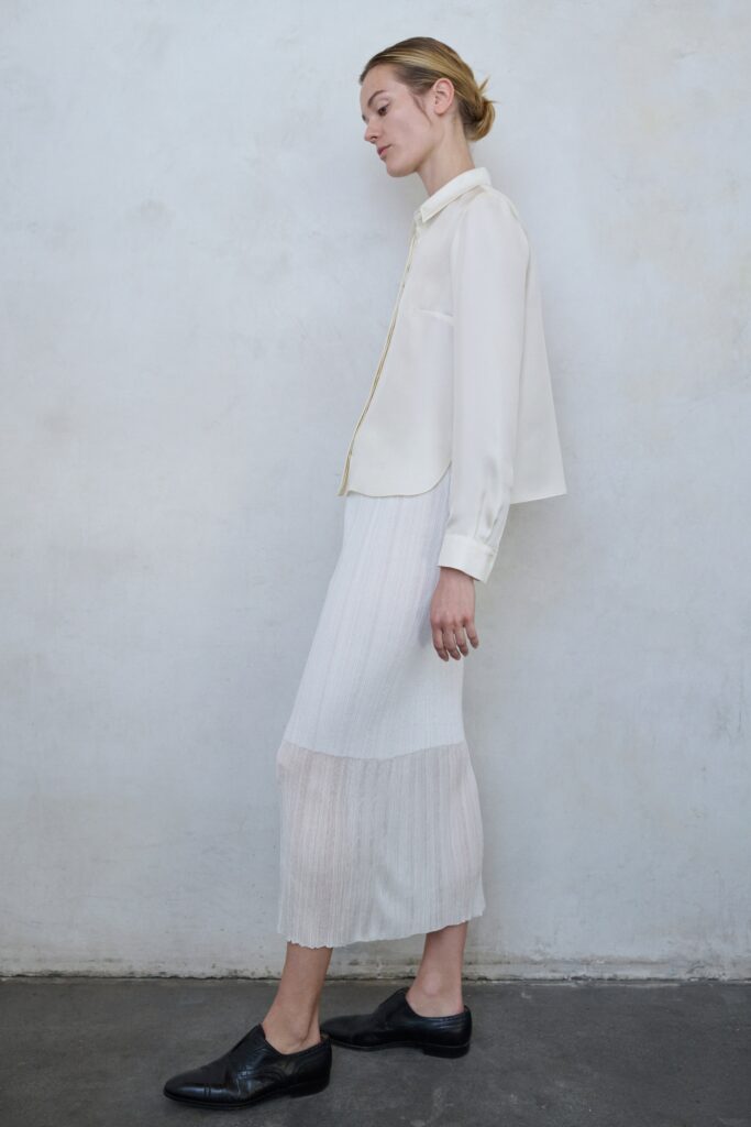 A relaxed white silk long-sleeve shirt paired with a pleated, tiered skirt.